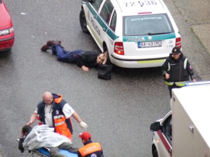 Un policía se protege detrás de un coche de los disparos de un desconocido, mientras los servicios de urgencias atienden a otro agente herido.