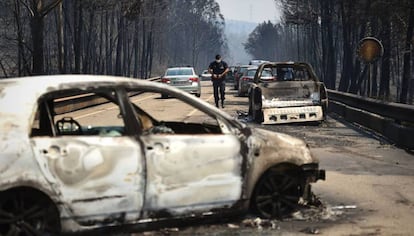 Un policía camina entre coches quemados.