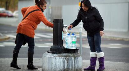 Aguasanta Quero y Toñi Rodríguez rellenan garrafas de agua en una fuente.