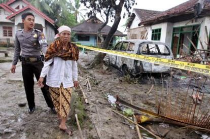 Un policía acompaña a Aminah, madre de uno de los muertos en el linchamiento del domingo, a su casa destruida en Pandeglang.
