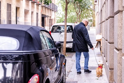 Un hombre camina con su perro por una acera estrecha del centro de Madrid, con coches aparcados.