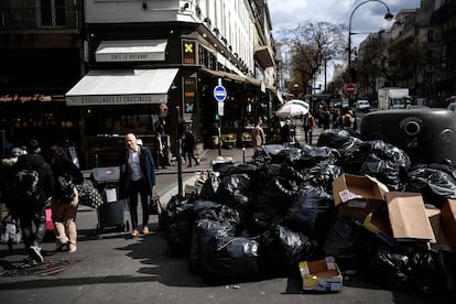 Pedestrians walk past a pile of garbage bags that have been piling up since waste collectors went on strike against the French government's proposed pensions reform, in Paris on March 15, 2023. 