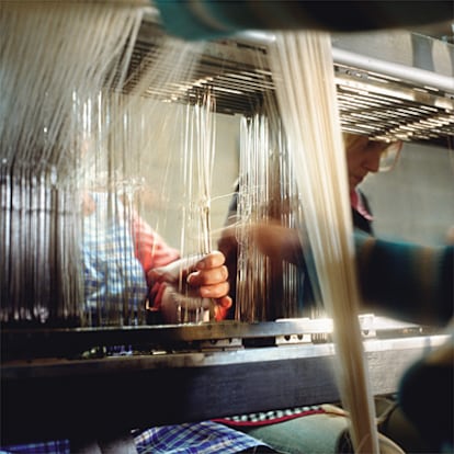 Unas manos pasando el hilo, un detalle del proceso textil que remite a tiempos más artesanales.