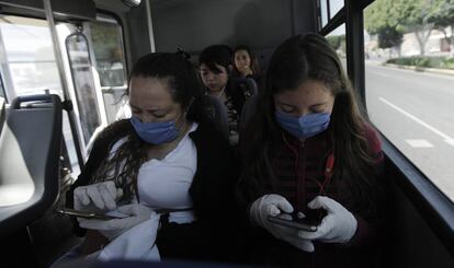 Dos mujeres con mascarillas y guantes usan su móvil en Querétaro, México.
