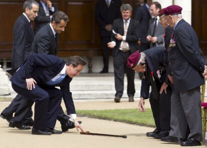 David Cameron recoge el bastón de un veterano condecorado en Londres, ante la mirada de Nicolas Sarkozy.