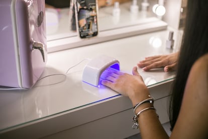 Una mujer ultima su manicura semipermanente bajo una lámpara.