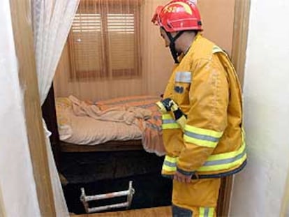 Un bombero observa el agujero que se abrió bajo la cama de la anciana que resultó herida grave.