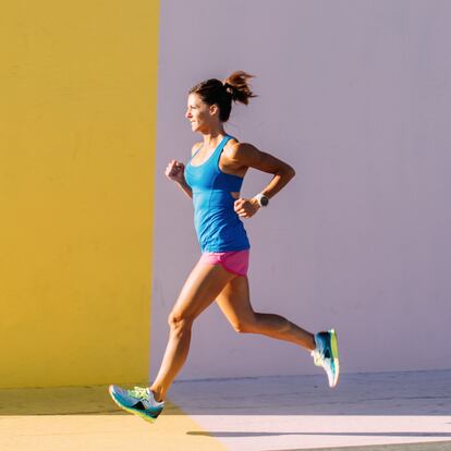 A woman runs against a colorful wall in the city. She has a determined look on her face while she picks up her stride in the summer sun.