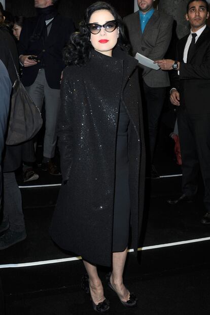 Dita Von Teese con total look negro, rojos rouge y gafas cat-eye en el desfile de Jean Paul Gaultier.