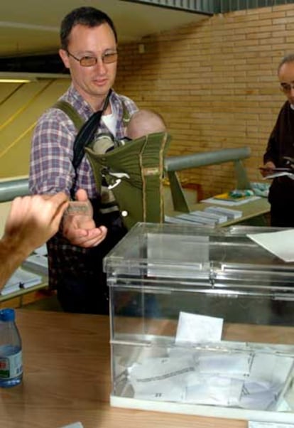 Un hombre, con su bebé a cuestas, se dispone a depositar su voto en un colegio electoral de la Garriga.