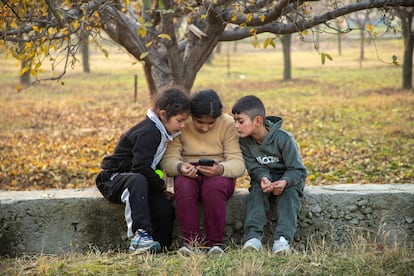 Kashmiri children playing games on a cell phone at an orchard on a cold autumn day in the outskirts of Srinagar city