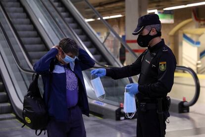 Un agente de la Policía Nacional ofrece mascarillas a una usuaria del metro de Madrid.