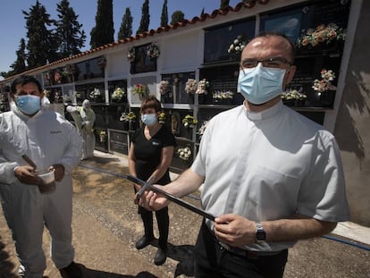 De izquierda a derecha, Leandro Cañaveras, sepulturero, con una jarra llena de ‘tierra santa’; Nieves Cuenca, hija de un hombre muerto de covid-19; y Alberto García, párroco de San Clemente, en el cementerio de la localidad.