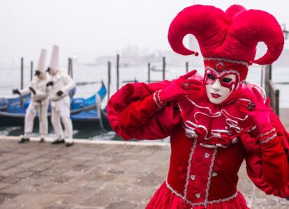 Un hombre con traje de carnaval posa delante de otros dos con máscaras tradicionales italianas, en Venecia (Italia).