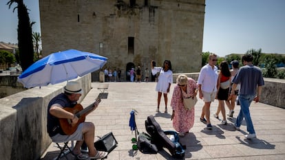 Un guitarrista toca en el Puente Romano de Córdoba, protegido del sol con una sombrilla, este domingo.