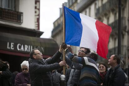 Tres personas colocan una bandera francesa ante el bar Le Carillon de París, Francia.