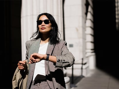 Un mujer mirando su reloj mientras camina por la calle.