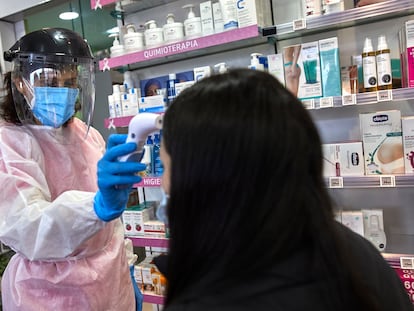 Una farmacéutica toma la temperatura a una mujer antes de realizarle un test de antígenos en una farmacia de Madrid (España), en febrero.