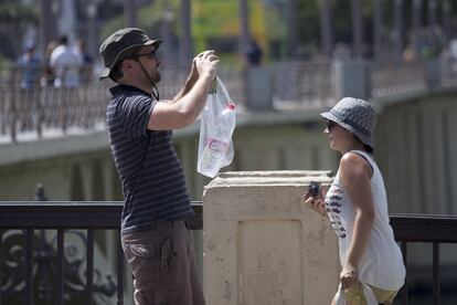 Dos turistas en Sevilla hacen fotos sin soltar la botella de agua que llevan en una bolsa.