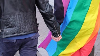 Una pareja se coge la mano con la bandera multicolor.