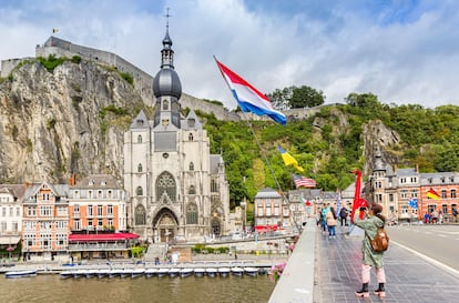 Turistas cruzando el puente Charles de Gaulle mientras fotografían la colegiata de Dinant (Bélgica).