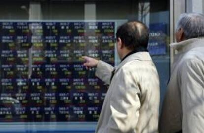 Dos viandantes observan varios valores burstiles en una pantalla en el centro de Tokio. EFE/Archivo