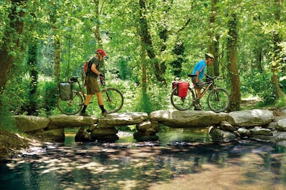 Unos ciclistas sortean un río en Galicia durante su peregrinaje por el Camino de Santiago.