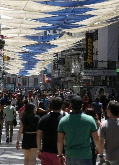 Ciudadanos de Madrid pasean por una calle céntrica, protegida del sol.