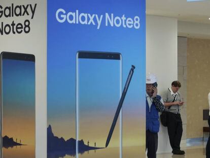 Varias personas utilizando sus teléfonos junto a un cartel publicitario del Galaxy Note 8 de Samsung. 