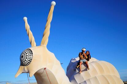 Dos festivaleros sentados en un vehículo iluminado con forma de caracol en el festival Afrikaburn celebrado en Tankwa Karoo, Calvinia (Sudáfrica).