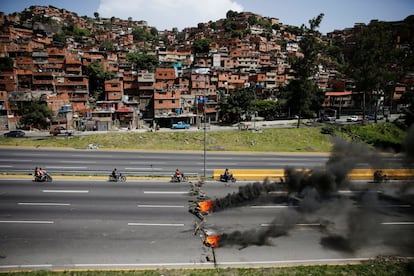Un grupo de motociclistas pasa junto a una barricada en llamas, en Caracas, el 26 de junio de 2017.
