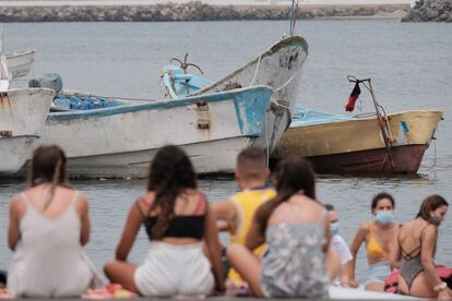 Bañistas frente a los cayucos amontonados en el muelle de Arguineguín, en Gran Canaria, donde han llegado a pernoctar bajo carpas más de 400 inmigrantes.