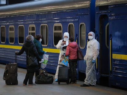 Trabalhadores com macacão de proteção verificam os documentos dos passageiros prestes a embarcar, na estação de Kiev, em um trem para Moscou.