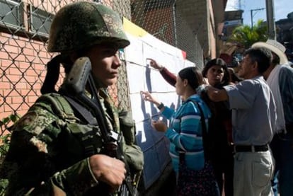 Un soldado monta guardia ante un colegio electoral de Medellín, mientras los votantes consultan las listas del censo electoral.