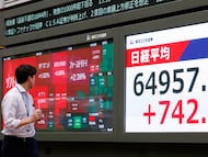 Una persona pasa junto a un panel de indicadores bursátiles en Tokio, Japón