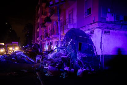 Vehculos destrozados y desplazados por la riada, iluminados por las luces de emergencia de cambiones de bomberos y otros vehculos de emergencia, en el centro de Paiporta, jueves 31 de octubre de 2024.