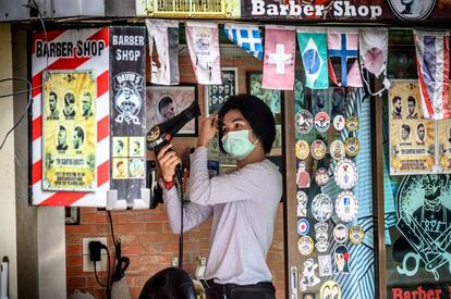 Un empleado de una barbería en Tailandia se arregla el pelo mientras espera la llegada del siguiente cliente.