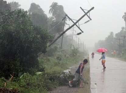 Varios residentes caminan bajo las fuertes lluvias al lado de un poste eléctrico inclinado después que el tifón Bopha afectase a la ciudad de Tagum, en la isla meridional de Mindanao.