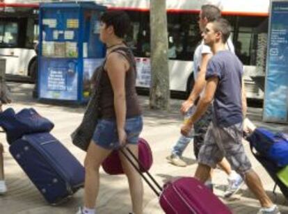 Varios jovenes turistas arrastran sus maletas camino a su hotel en las populares Ramblas de Barcelona. 