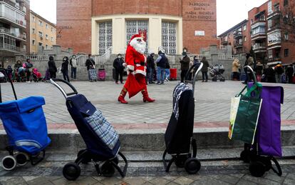 Un hombre vestido de Santa Claus camina entre una fila de personas que esperan recibir alimentos de una ONG en Madrid (España), el 24 de diciembre.