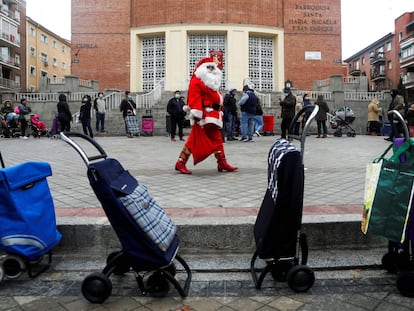 Un hombre vestido de Santa Claus camina entre una fila de personas que esperan recibir alimentos de una ONG en Madrid (España), el 24 de diciembre.