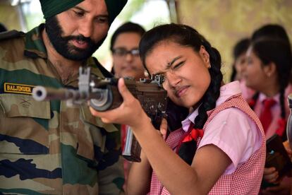 Un soldado del ejército indio observa a una estudiante que apunta con un rifle de asalto durante la exposición 'Conozca a su ejército', en Rajasthan (India), este martes.