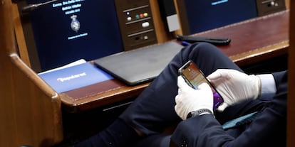 Un diputado consulta su móvil con unos guantes durante el pleno extraordinario para explicar la declaración del estado de alarma.