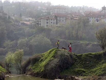 Dos caminantes, con las casas del barrio de La Arboleda de Bilbao al fondo.