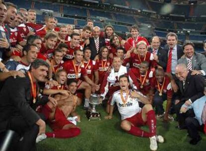 Los sevillistas, con Juande Ramos a la izquierda y José María del Nido en el centro, posan sobre el cesped con el trofeo.