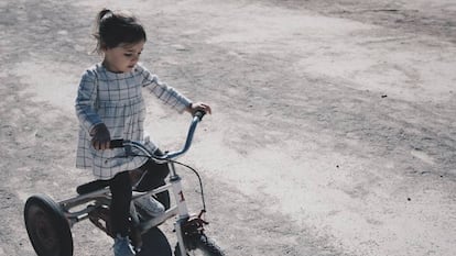 Una niña va con su tríciclo por la calle.