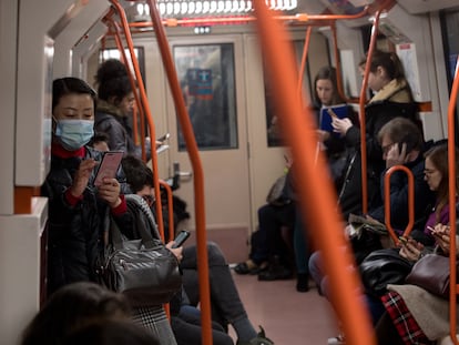Mulheres no metrô de Madri usando máscaras enquanto olham para o celular.