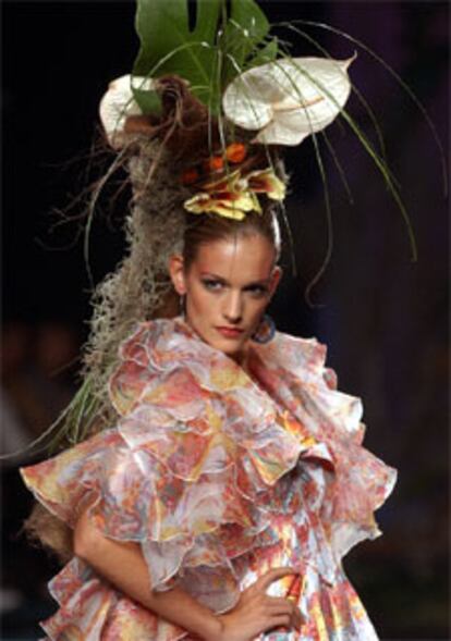 Los motivos florales son una constante en los diseños de Montesinos. En la imagen, una modelo exhibe un vestido y capa avolantada en estampado <i>frenesí</i> y tocado realizado con flores y plantas.