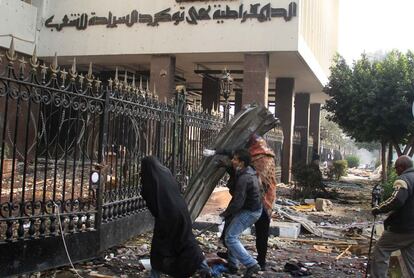 Los manifestantes se protegen tras un improvisado escudo metálico mientras arrojan piedras contra la policía militar que se halla en el interior del Parlamento, en El Cairo.