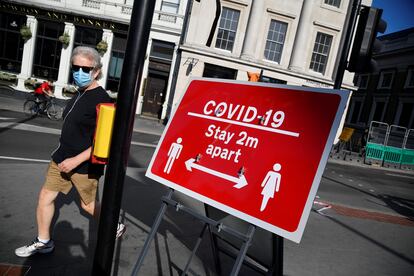 Un hombre camina junto a un cartel en Londres que pide que se mantengan dos metros de distancia entre personas.